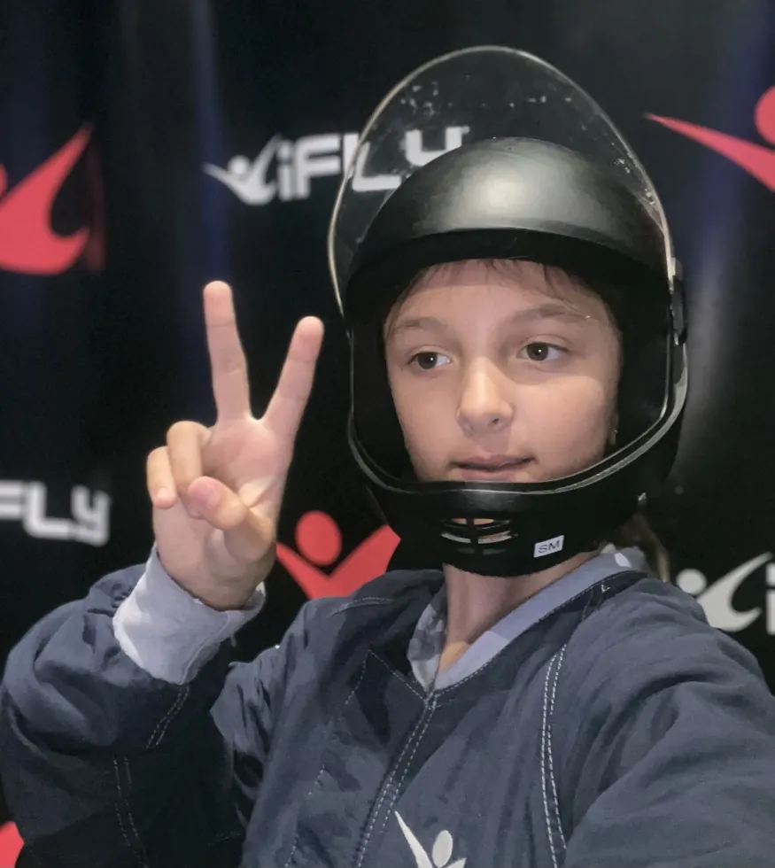 Ruby in a flight helmet and jumpsuit throwing a peace sign at the wind tunnel