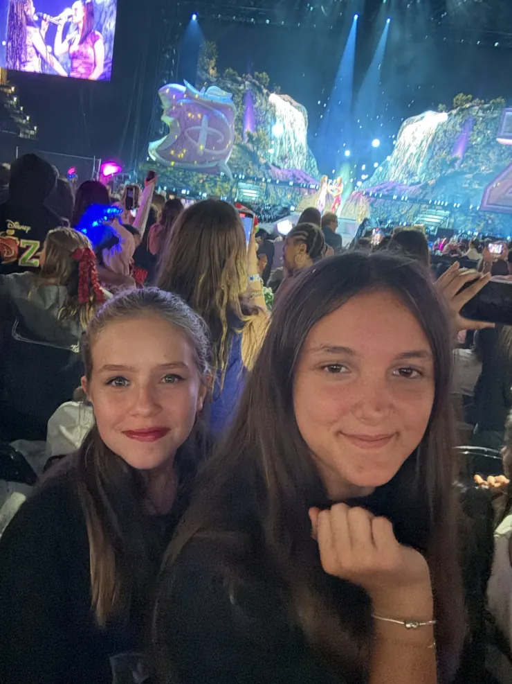Ruby and a friend in the crowd at an arena show, stage lit behind them