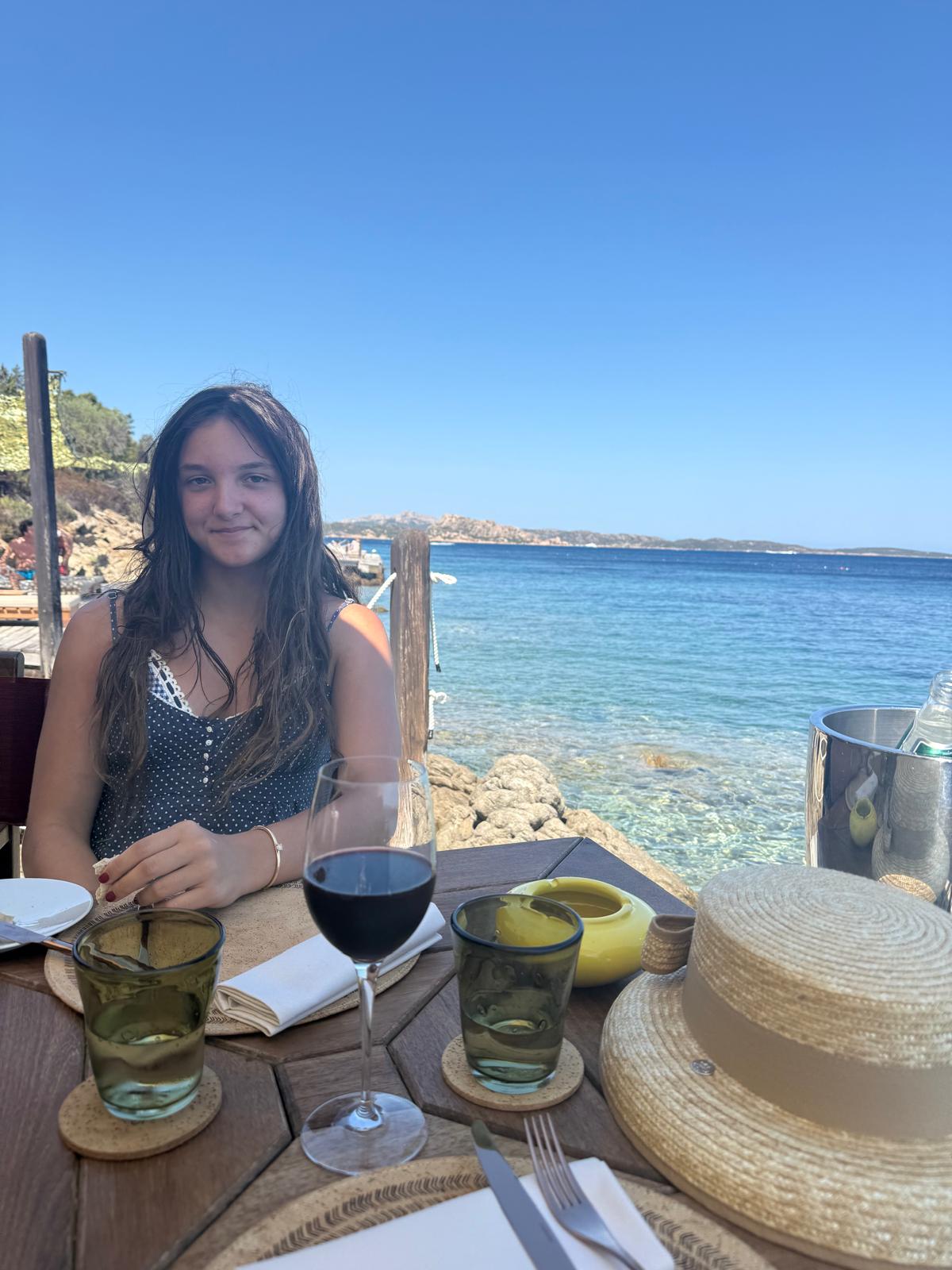 Ruby at a table by clear blue sea in Sardinia